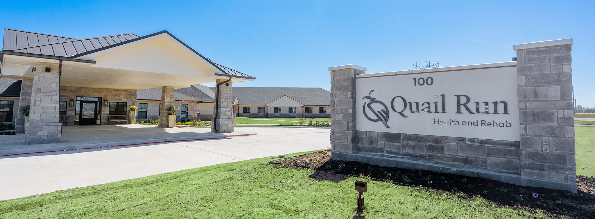 The exterior entrance of Quail Run Health and Rehab, a modern nursing home and elderly care center. The building features a covered drop-off area, stone pillars, and a large sign with the facility name. This skilled nursing and senior living facility offers a welcoming and professional environment for residents seeking compassionate long-term care.