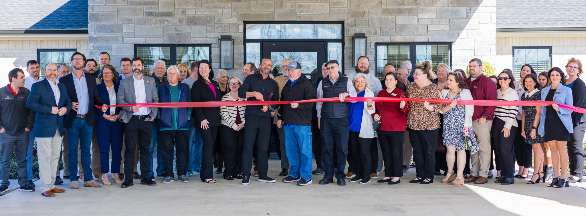 A large group gathers in front of a nursing home for a ribbon-cutting ceremony, celebrating the opening of a new facility that offers rewarding careers in healthcare. This event highlights opportunities for health care jobs and nursing home jobs within a compassionate and professional senior care environment.