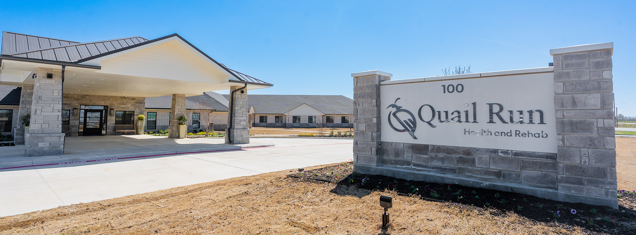 The exterior entrance of Quail Run Health and Rehab, a modern nursing home and elderly care center. The building features a covered drop-off area, stone pillars, and a large sign with the facility name. This skilled nursing and senior living facility offers a welcoming and professional environment for residents seeking compassionate long-term care.