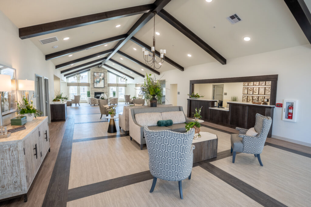 A spacious and elegantly designed common area inside a nursing home, featuring high ceilings, modern furnishings, and abundant natural light. This senior living facility offers skilled nursing services in a warm, inviting elderly care center where residents can relax and socialize in comfort.